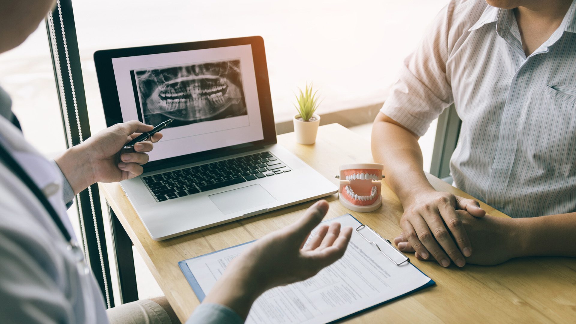 Dentists are discussing dental problems at report x-ray image on laptop screen to patients.