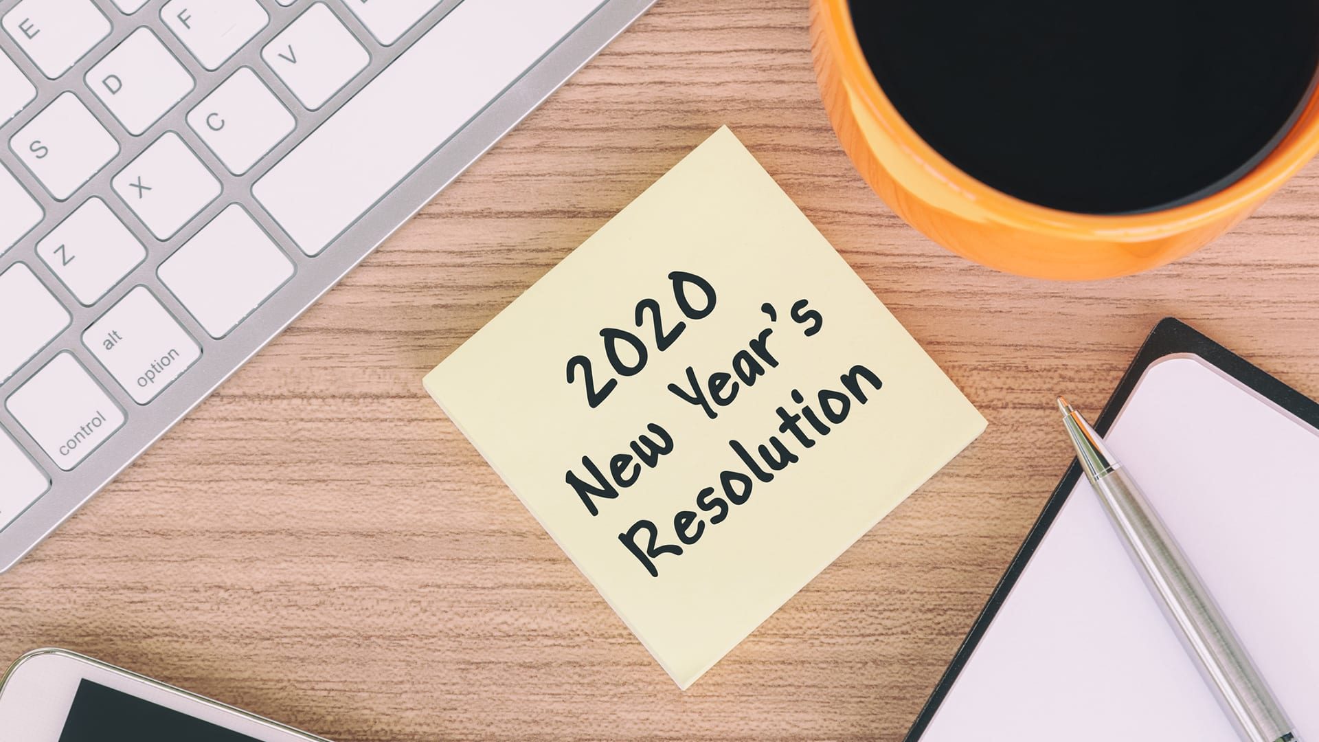 New Year concept - 2020 New Year's Resolution on paper note with coffee, computer keyboard, smartphone, pen and note pad.