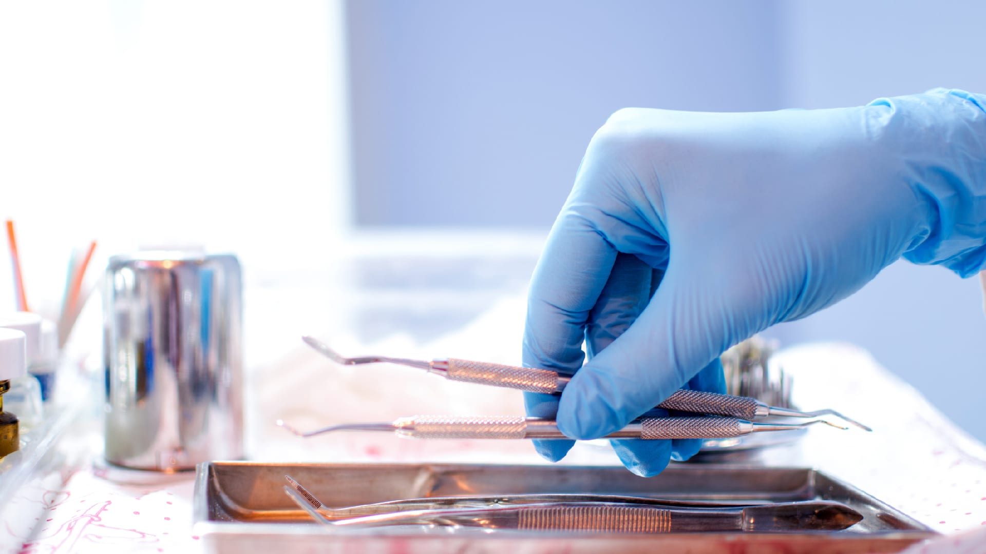 Close up of hand in surgical glove holding dental tools.